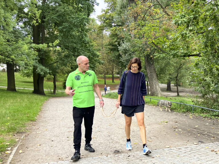 Ein Mann mit grünem T-Shirt läuft mit einer Frau durch einen Park. Sie sind mit den Händen über ein Band verbunden.